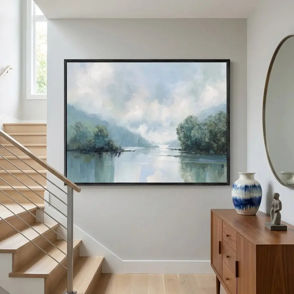 Framed landscape painting on a wall above a wooden staircase with a vase and sculpture on a side table.