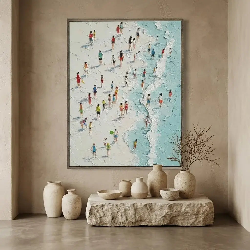 Framed artwork of a beach scene with people on a beige wall above a stone shelf with decorative vases.