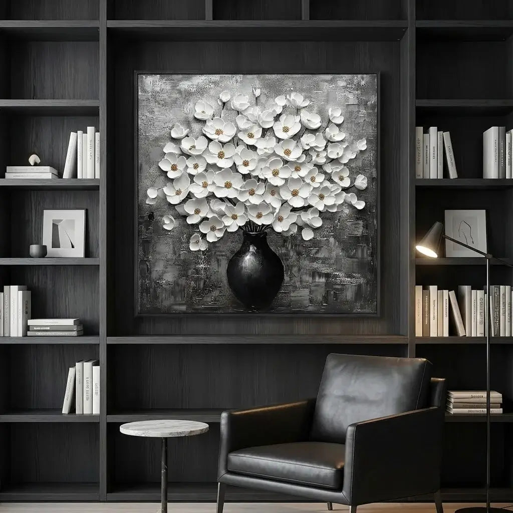 Framed artwork of white flowers in a black vase on a dark wall above a black armchair.