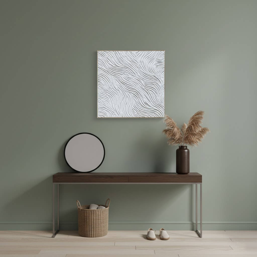 Minimalist interior with a square painting, vase with dried plants, and small table against a green wall.