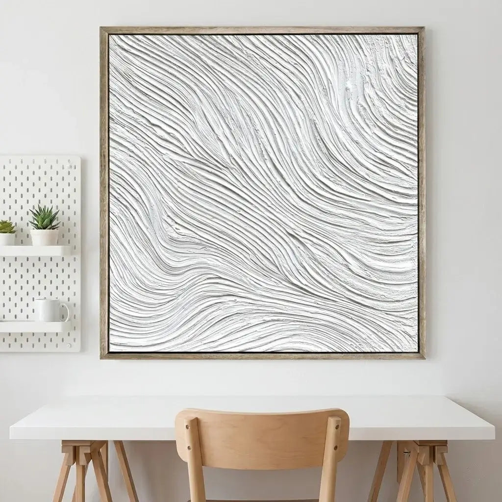 Abstract wall art with wavy lines in a wooden frame on a white wall above a table and chair.