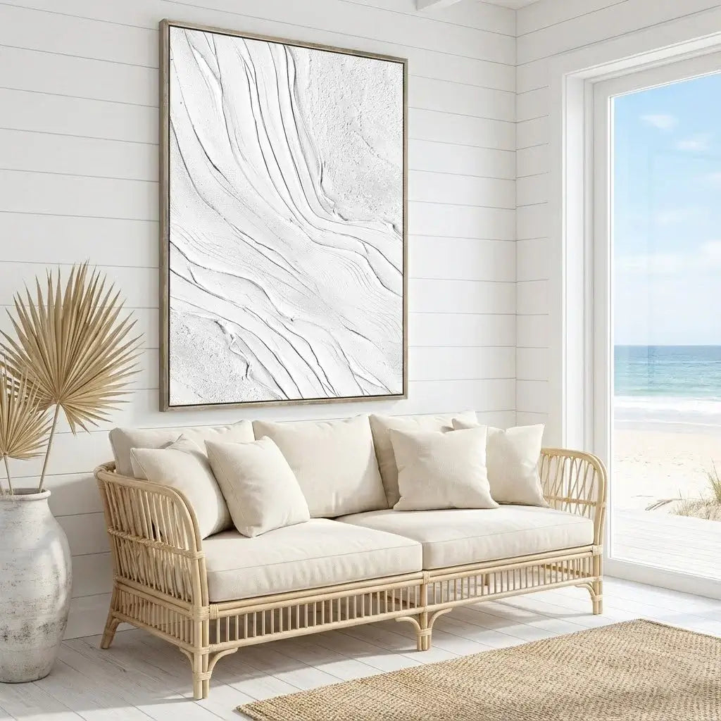 Beige sofa with white cushions in a room with a large abstract painting on the wall and a window showing a beach view.