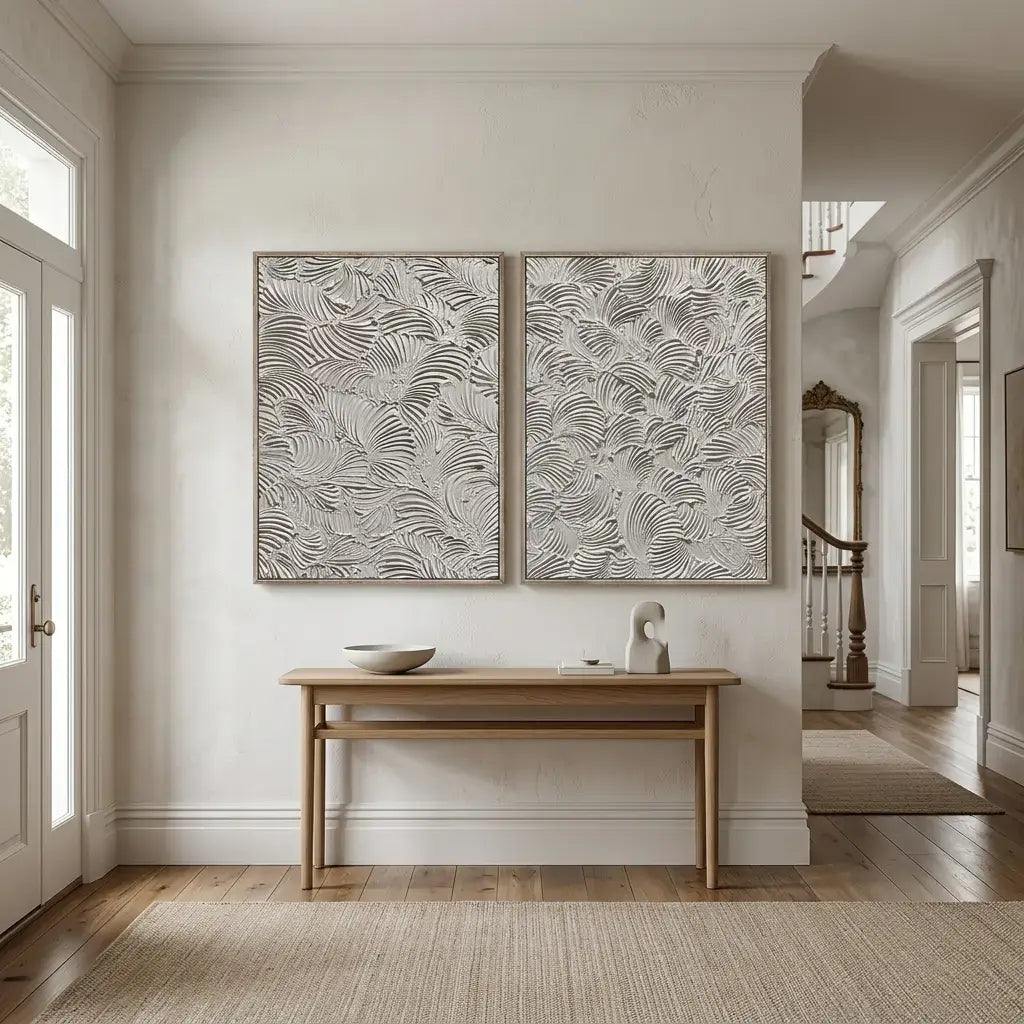 Two abstract wall art pieces above a wooden table in a room with light-colored walls and wooden flooring.