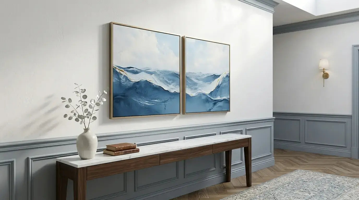 Two abstract blue artworks on a white wall above a wooden bench with decorative items.